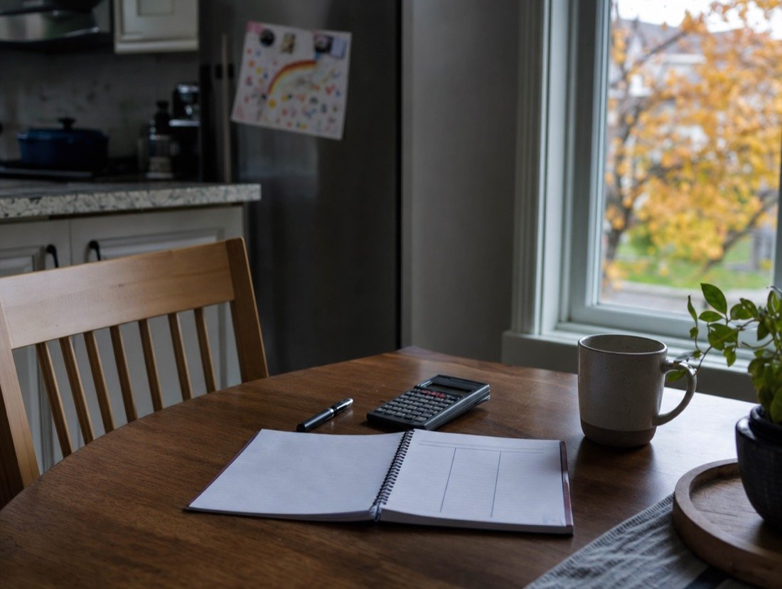 A kitchen table with a notebook and calculator, set out for planning a monthly budget