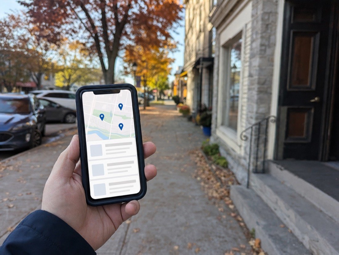 A phone showing local search results on a tree-lined Milton street of limestone storefronts
